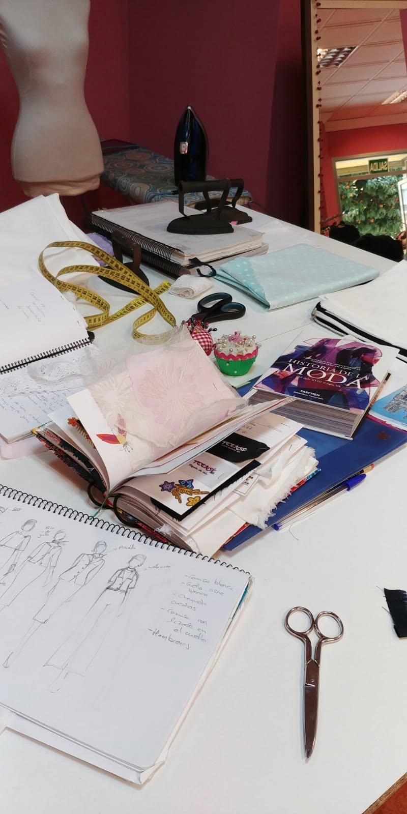 Mesa de trabajo del taller de costura Hilillos con patrones, telas y herramientas